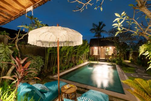an outdoor swimming pool with an umbrella and a house at Clamonic Villa Ubud - Monthly Rental Available in Sukawati