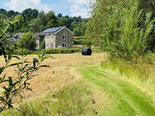 an old house with a large black barrel in a field at Maesyfelin Isaf Apartment in Llanybydder