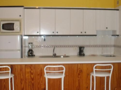 a kitchen with white cabinets and a sink and two stools at Apartamentos La Banda in Playa de Santiago
