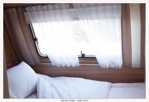 a bedroom with a bed and a window with white curtains at Ras Hasita in H̱aẕeva