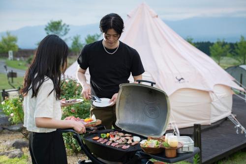 a man and a woman preparing food on a grill at くじゅう花公園 グランピングパーク花と星 in Kuju