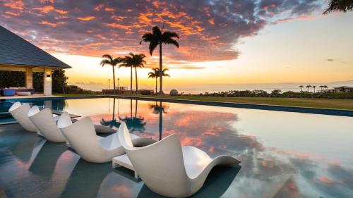 a pool with white chairs and a sunset at MAUNA KEA BEACH ESCAPE Luxurious home in private community with Heated Private Pool and Spa Detached Ohana Suite in Waimea