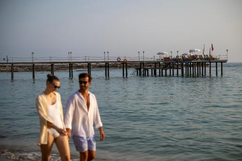 a man and woman walking on the beach near the water at Oz Hotels Incekum Beach in Alanya