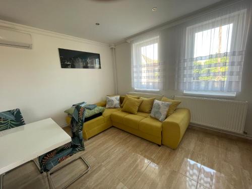a living room with a yellow couch and two windows at Anett Wellis Apartman Poroszló in Pusztavacs