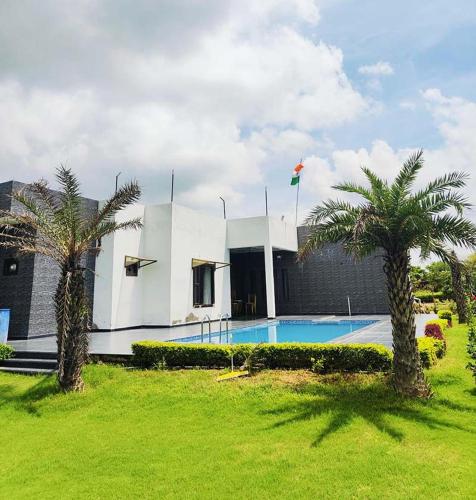 a house with a swimming pool and two palm trees at Evergreen Aravali Farmhouse in Jāmb