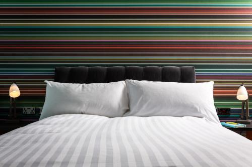 a bed with white pillows in front of a striped wall at Village Hotel Warrington in Warrington