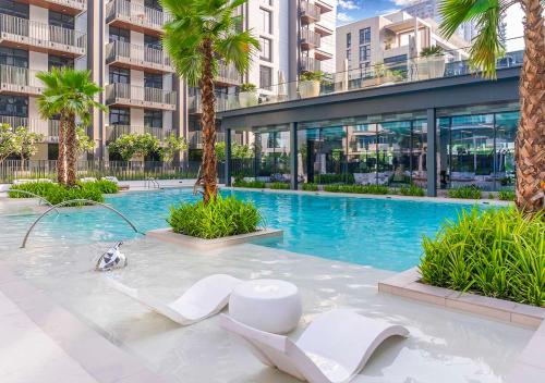 a swimming pool with palm trees and a building at Royal Vista - Luxury 1BR Apartments at Kensington Waters in Dubai