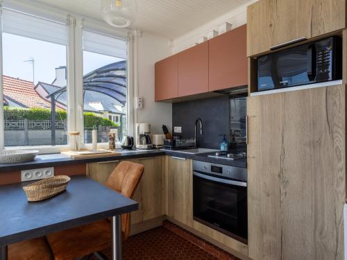 une cuisine avec des armoires en bois, une table et une fenêtre dans l'établissement Petite Maison Cosy, à Trégastel