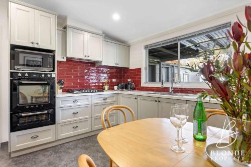 a kitchen with white cabinets and a wooden table at Journeyman's Cottage in Ballarat