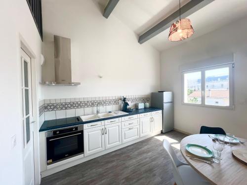 a kitchen with white cabinets and a table and a window at Le Spacieux - Royan, Wifi & Balcon in Royan