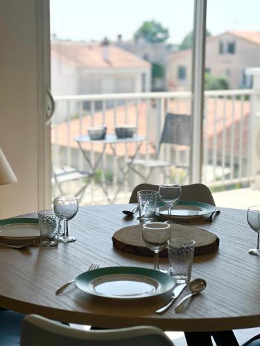 a wooden table with plates and wine glasses on a balcony at Le Spacieux - Royan, Wifi & Balcon in Royan