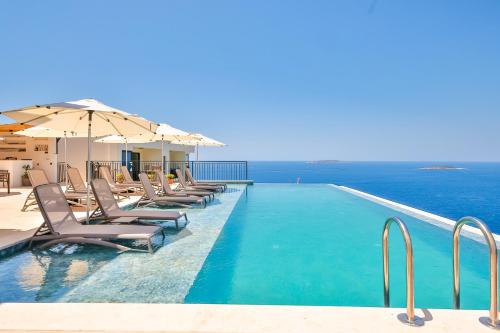 a swimming pool with chairs and umbrellas and the ocean at Lyxos Hotel in Kas