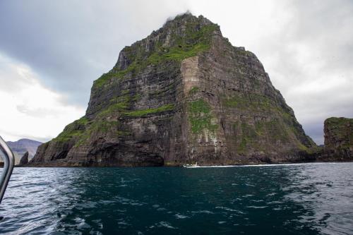 a large mountain in the water with a boat at VILLA ORANGE - Spacious piano home in Klaksvik in Klaksvík