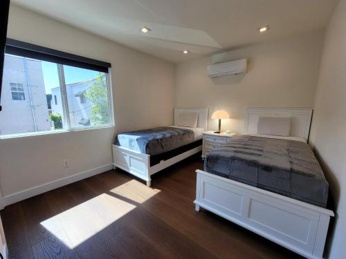two beds in a room with a window at Newly built three bedroom close to Rodeo Drive Hollywood Downtown and Beaches Close to attractions in Los Angeles