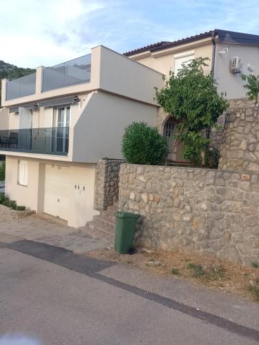 a house with a stone wall and a green trash can at Natalija apartmani in Sveti Juraj