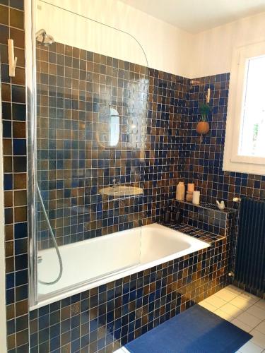 La salle de bains est pourvue de carrelage bleu, d'une baignoire et d'un lavabo. dans l'établissement Appartement proche de l'aéroport de Nantes, à Saint-Aignan-Grand-Lieu