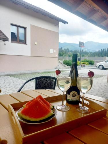 a bottle of wine and a plate of watermelon and two glasses at Apartmán pod Sivým vrchom in Zuberec