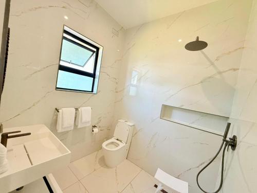 a bathroom with a toilet and a sink and a window at 19 On BayNoakes Boutique in Harare