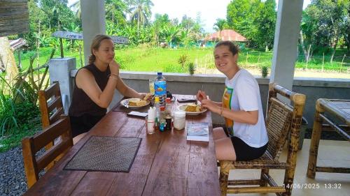 two women sitting at a wooden table with food at Ariel Bungalow Tetebatu in Tetebatu