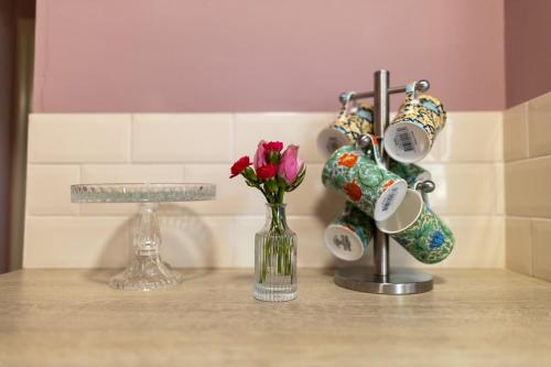 a counter top with a vase of flowers and cups at Gate Lodge - Sleeps 4 - Near Belvoir Castle in Knipton