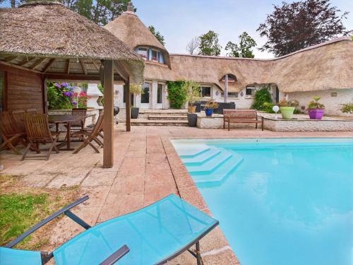 une cour arrière avec une piscine et une maison au toit de chaume dans l'établissement Piscine chauffée, Grand jardin, maison pour 8, à Pleuven