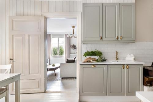 a kitchen with white cabinets and a living room at Historic apartment near the city by the water in Solna