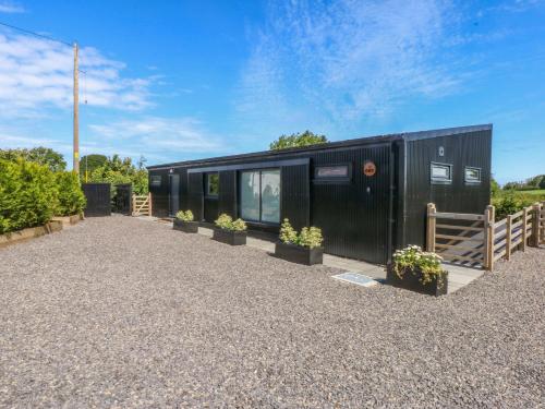 a black tiny house sitting on top of a gravel lot at Y Cwt in Moelfre