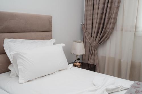 a bed with white sheets and a lamp on a table at The One Boutique Hotel in Muçaj