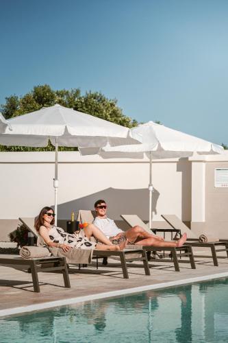 two people laying on lounge chairs next to a swimming pool at Eleia Domos in Monopoli