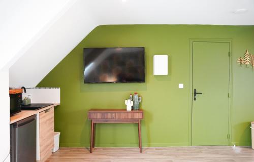 a green kitchen with a table and a tv on the wall at Jungle Room - Studio avec spa privé in Quéven