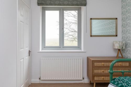 a white room with a window and a wooden dresser at Lower Barn House at Westerlands Farm Sleeps 11 in Graffham