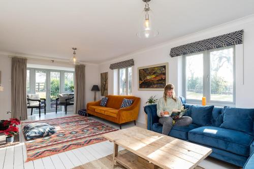 a woman sitting on a blue couch in a living room at Lower Barn House at Westerlands Farm Sleeps 11 in Graffham