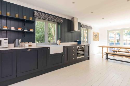 a large kitchen with black cabinets and a table at Lower Barn House at Westerlands Farm Sleeps 11 in Graffham