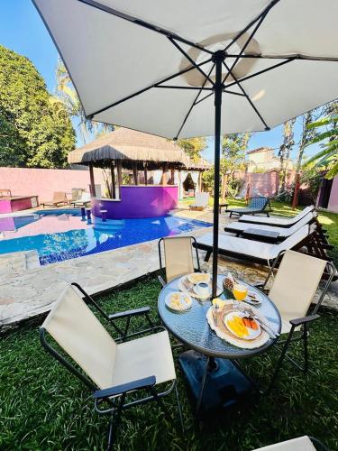 een tafel met een parasol en stoelen naast een zwembad bij Vila Bardot in Barra do Sahy