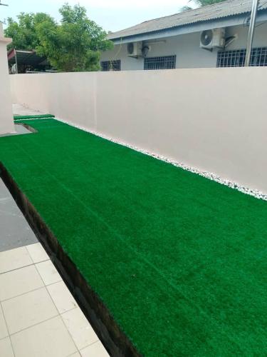 a fake green lawn in front of a white fence at Cream Roof Homestay in Gua Sai