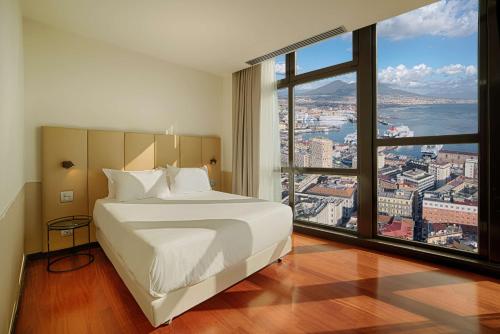 a bedroom with a white bed and a large window at NH Napoli Panorama in Naples