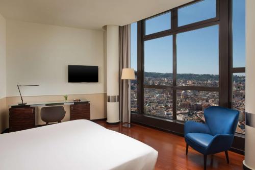 a bedroom with a bed and a tv and a blue chair at NH Napoli Panorama in Naples