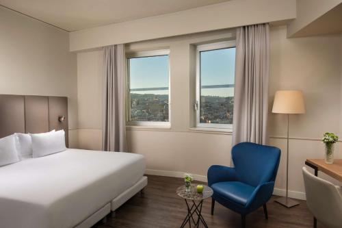 a hotel room with a bed and a blue chair at NH Napoli Panorama in Naples