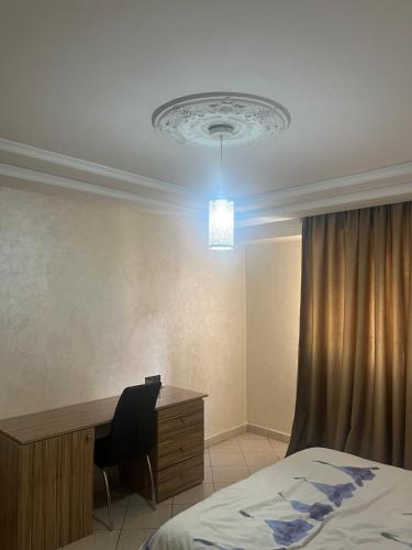 a bedroom with a desk and a bed and a chandelier at Appartement proximité Gare TGV 3 in Kenitra