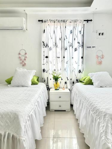 Casa Eme Hostal في كارتاهينا دي اندياس: سريرين في غرفة بجدران بيضاء وستائر