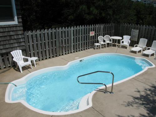 a swimming pool with chairs and a table and a fence at Reminiscent in Nags Head