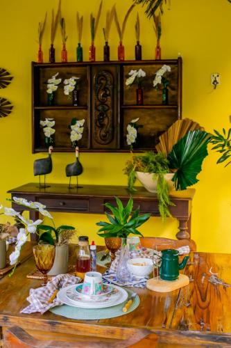 a dining room table with dishes and plants on a yellow wall at Chalés serra linda in Bananeiras