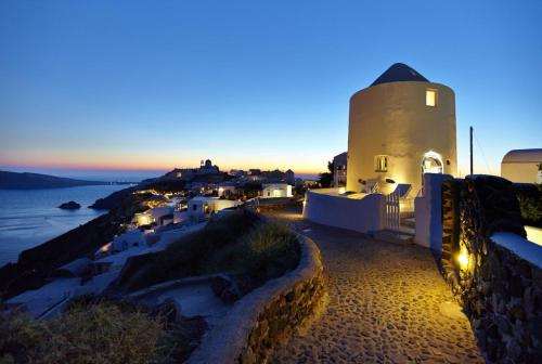 a lighthouse on the coast of a town at night at Elegant Santorini House 1 Bedroom Villa Windswept House Amazing Caldera View & Outdoor Hot Tub Oia in Thólos