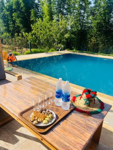 a picnic table with a plate of food and water bottles at Al Nakheel - Ferme Spacieuse avec Grande Piscine Privée et Espace Vert in Kenitra