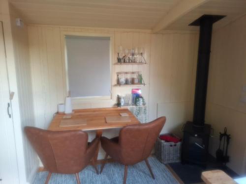 a table and chairs in a room with a stove at Hill Top Hideaway Shepherds Hut with Hot Tub in Woodham Mortimer
