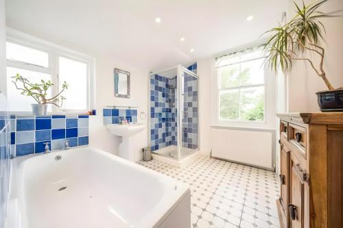 a bathroom with a white tub and blue tiles at EEJs Luxe 5 Bed Home - Greenwich in London