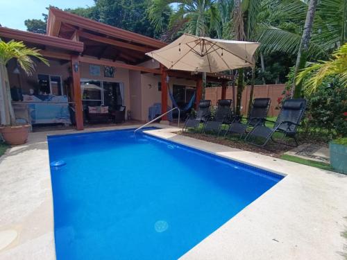 a blue swimming pool with an umbrella and chairs at Alma y Paz Beach House in Bejuco