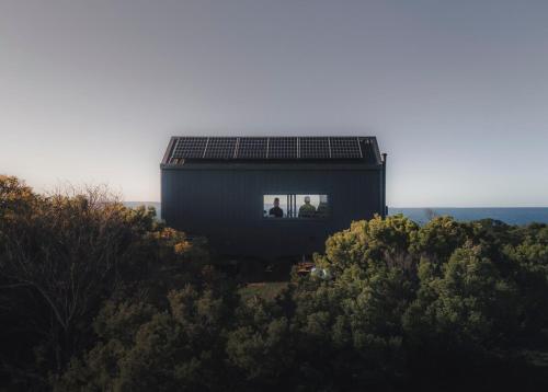 a black house with two people sitting in the window at Beach Front Off-Grid Cabin on Kangaroo Island - Xanthe in Antechamber Bay