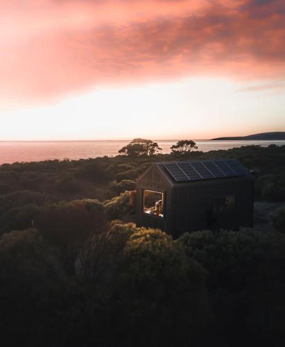 a person is sitting in the window of a small house at Beach Front Off-Grid Cabin on Kangaroo Island - Xanthe in Antechamber Bay