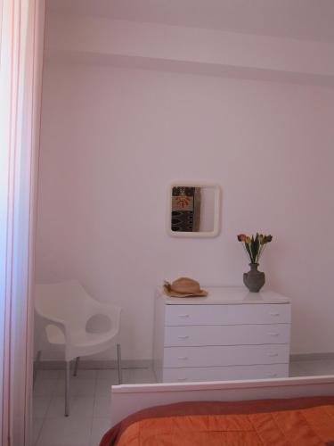 a white bedroom with a white dresser and a chair at Palms Villa in Scopello